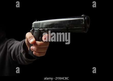 Armed hand with a gun closeup, man holding a pistol on dark background. Danger and crime concept Stock Photo
