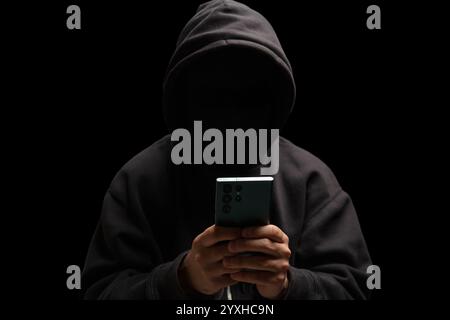 Hacker in black hood holding a mobile phone, Scam cyber crime concept Stock Photo