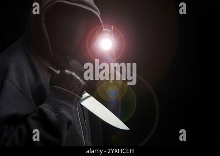 Criminal holding a knife, hooded man holding a weapon in gloved hand, black background, armed attack concept. Stock Photo