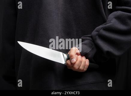 Criminal hiding a knife behind his back, man holding a weapon closeup view, armed attack concept. Stock Photo