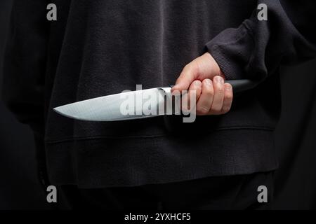 Criminal hiding a knife behind his back, man holding a weapon closeup view, armed attack concept. Stock Photo