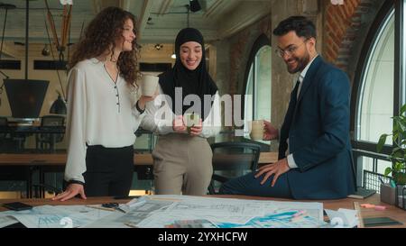 Team architects contractors engineers business colleagues Arabian Muslim Caucasian businessman businesswomen drink coffee break happy relaxed man Stock Photo