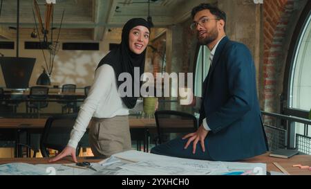 Two architects contractors engineers colleagues architecture project Arabian muslim designers man woman in hijab discuss blueprint draft of office Stock Photo
