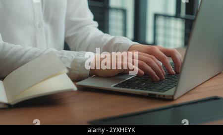 Hands typing computer laptop programming at workplace notebook planning business tasks unrecognizable woman female businesswoman student writing notes Stock Photo