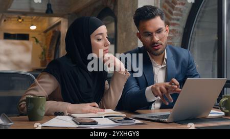 Two business colleagues co-workers talk discuss corporate work at office cafe multiracial male female employees Indian man muslim woman in hijab Stock Photo
