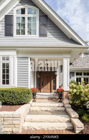 A front door and covered porch detail on a home with grey siding, white trim, red brick, a wooden front door. Stock Photo