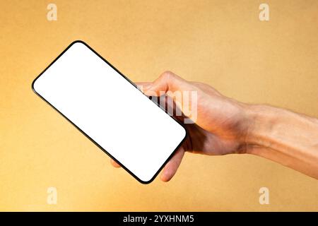 Man's hand holding a generic modern smartphone with blank white screen, empty display app mockup template, copy space, new mobile phone on minimal bac Stock Photo