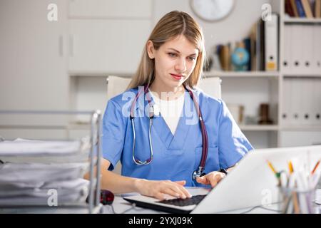 Focused woman doctor working in medical office using laptop Stock Photo