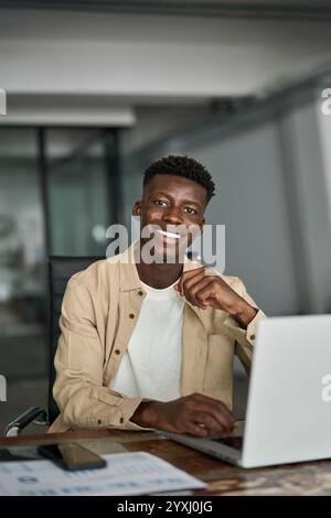 Vertical portrait of happy young African business man with laptop working in office. Stock Photo