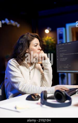 Freelancer doing software debugging using computer, checking errors in lines of code displayed on PC monitors. IT professional in apartment fixing coding issues using desktop PC Stock Photo