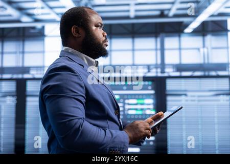 Supervising manager in data center implements backup solutions to protect against data loss using tablet, ensuring efficiency. High tech establishment IT expert resolving technical issues using device Stock Photo