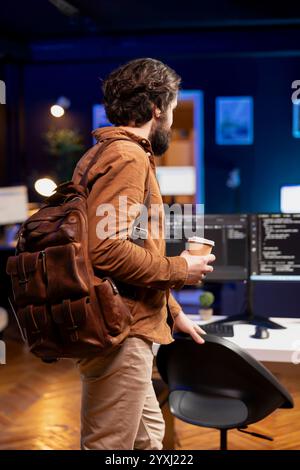 Programmer with disposable cup of coffee entering office to implement security measures, protecting company systems and data. IT worker starting job shift, testing and debugging code Stock Photo
