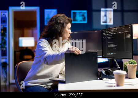 Teleworking software developer working from home opening laptop to write programs in Java programming language. Woman checking code displayed on computer screen, sitting at desk chair Stock Photo