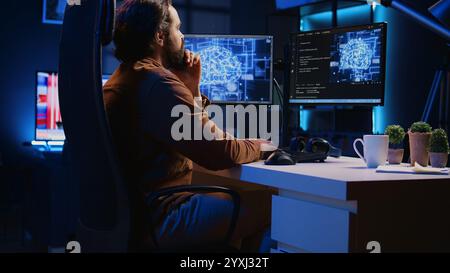 Freelancing programmer writes code on desktop PC to visualize artificial intelligence neural networks. Self employed man runs AI script on computer from apartment office, jib down shot Stock Photo