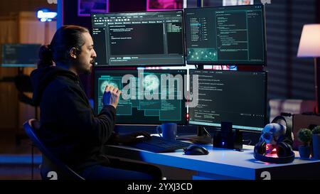 Hacker in secret hideout typing on keyboard, trying to hide online activity after stealing data. Scammer attacking victims computers using malware while trying to avoid being detected, camera A Stock Photo