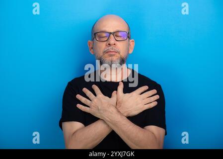 Bearded, bald man wearing prescription glasses and a black shirt with his arms crossed on his chest. Confident and focused. Studio shot. Stock Photo