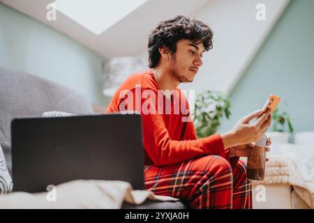 Young man using phone and laptop in cozy living room Stock Photo