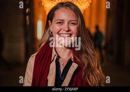 Smiling young woman with long blonde hair and a red scarf, standing at night under festive lights, looking directly at the camera with a happy expression, Lady with optimistic attitude staring front. High quality photo Stock Photo