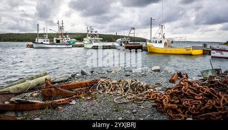Fishing boats in a harbor with rusty chain and old rope in the foreground in Nova Scotia Canada Stock Photo