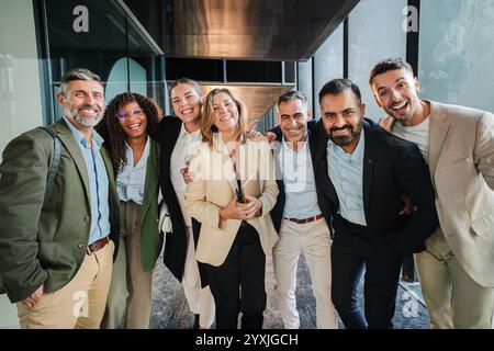 Diverse group of smiling business professionals standing together in office corridor, dressed in formal attire, celebrating teamwork, success, corporate unity and collaboration while posing happily. High quality photo Stock Photo