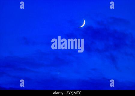 Conjunction of the waxing crescent Moon with Venus in clouds in the deep blue twilight sky. Stock Photo