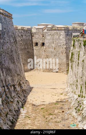 A narrow, rocky path leads to a castle. The castle is surrounded by a wall and has a few windows. The path is overgrown with weeds and there is a smal Stock Photo