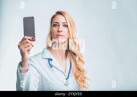 Young female doctor using a smartphone app for remote patient monitoring and ai-powered diagnostics, revolutionizing healthcare with technology Stock Photo