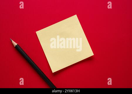 Yellow blank sticky note and pencil on red background Stock Photo