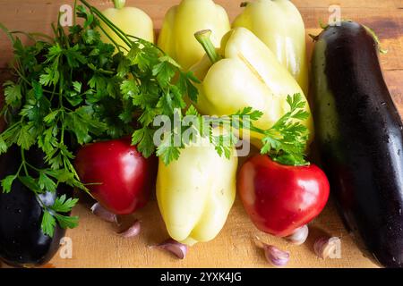 A vibrant collection of assorted vegetables, including peppers, eggplants, garlic, and fresh cilantro, is arranged beautifully on a wooden cutting boa Stock Photo