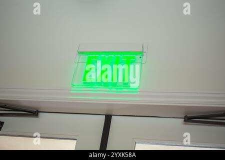 A view of a green lit exit sign above a doorway of a building. Stock Photo