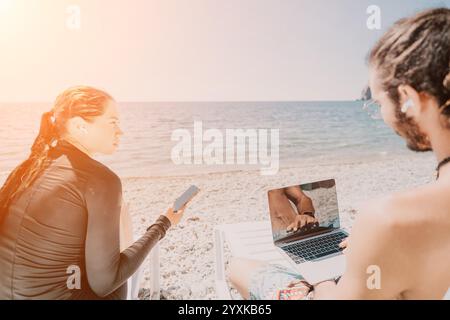 Couple Beach Laptop Working Remotely - Two people work on laptops while sitting on a beach. Stock Photo