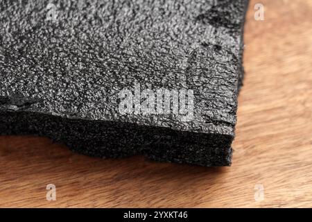 Black porous packaging foam with textured surface for secure shipping of fragile items. Placed on wooden background Stock Photo