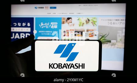 In this photo illustration, a person is holding a cellphone with the logo of Japanese company Kobayashi Pharmaceutical Co. Ltd. in front of business webpage. Stock Photo