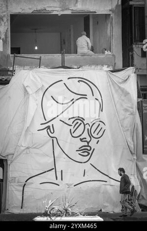 A large black-and-white mural of a woman wearing sunglasses drapes over a construction site in Alexandria, Egypt, with a passerby. Stock Photo