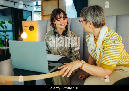 Female teacher assisting a student with their work in a contemporary learning space, highlighting the importance of mentorship and technology in educa Stock Photo