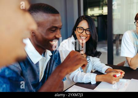 A group of university students laughing and collaborating at a table, showcasing friendship and teamwork during a study session. Stock Photo