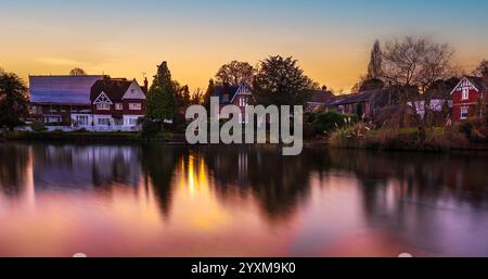 Traditional English house reflecting on a pond at sunset in Lindfield, West Sussex. Long exposure captures serene village charm. Stock Photo