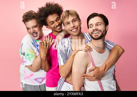 Four individuals express joy and pride in their vibrant, colorful outfits against a pink backdrop. Stock Photo