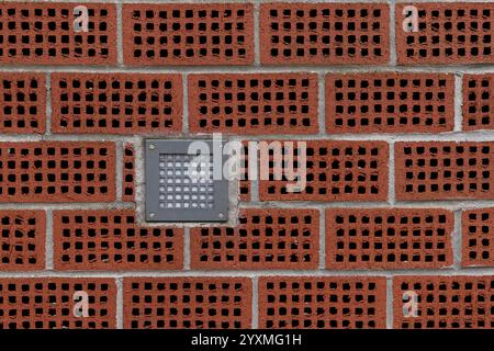 A textured brick wall features hollow red bricks arranged in a pattern, with a square light fixture mounted in the center, offering a modern design touch. Stock Photo