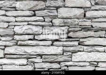 an aged stone wall, with irregularly shaped stones stacked horizontally to create a rugged facade. Stock Photo