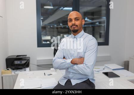 Confident young African American man, proudly posing at an office with crossed arms, portrait shot. Professionalism and expertise in business concepts Stock Photo
