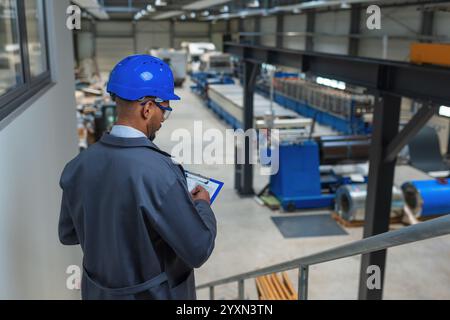 Young engineer programmer using tablet and graphs data to check factory machinery production and work procedure, rear view. Industry career concept. Stock Photo