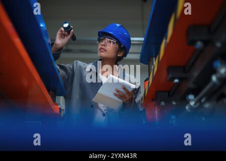 Indian woman engineer working in a production line, examining automated machinery work and writing down a planning checklist. Stock Photo