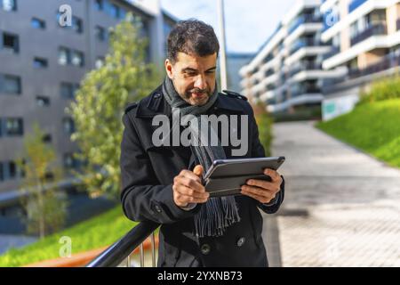 Businessman in casual winter clothes using digital tablet standing outdoors in the city in winter Stock Photo