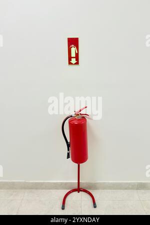 A red fire extinguisher placed below an exit sign on a white wall Stock Photo
