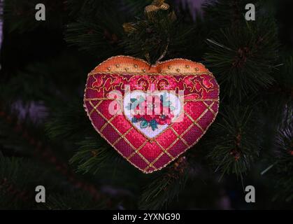 Cross stitched Christmas Timeless Elegance ornament on to a Christmas tree. This red heart shape Christmas ornament embroidered and made by myself. Stock Photo