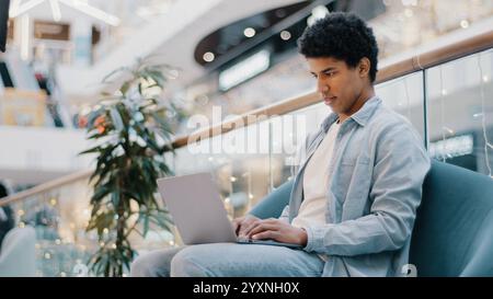 Relaxed serious busy millennial african ethnic student freelancer businessman using laptop device leaning on sofa in office company man focused Stock Photo