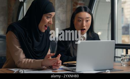 Multiracial women business colleagues multiethnic businesswomen girls Korean Asian worker manager Muslim female in hijab together working laptop shock Stock Photo