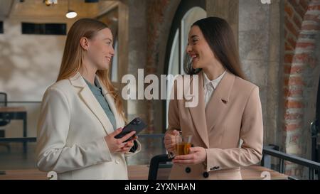 Two happy smiling talking Caucasian women girls office workers female managers businesswomen business friends smile talk conversation work break Stock Photo