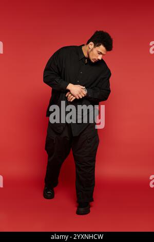 Man in black clothing stands confidently against a red backdrop. Stock Photo
